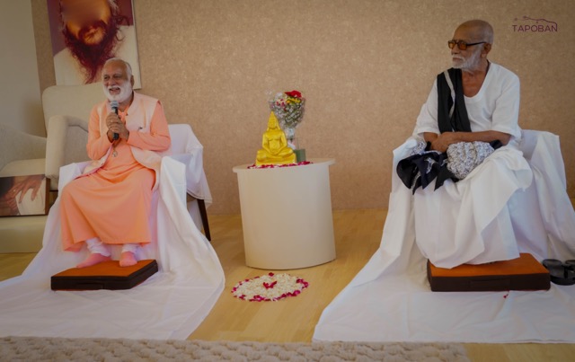 Swami Anand Arun speaking beside Pujya Morari Bapu in the ashram meditation hall